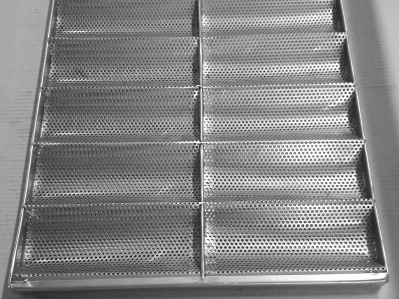 Vedere de detaliu asupra orificiilor de 3 mm ale tăvii din inox AISI 304 pentru baghete. Designul perforat cu 14 canale asigură circulația optimă a aerului pentru obținerea unei cruste perfecte, fiind un echipament indispensabil în orice brutărie profesională.