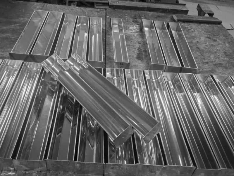 Set de tăvi și forme de terină din inox reflexiv, finisate profesional și aliniate pe bancul de lucru din atelier.