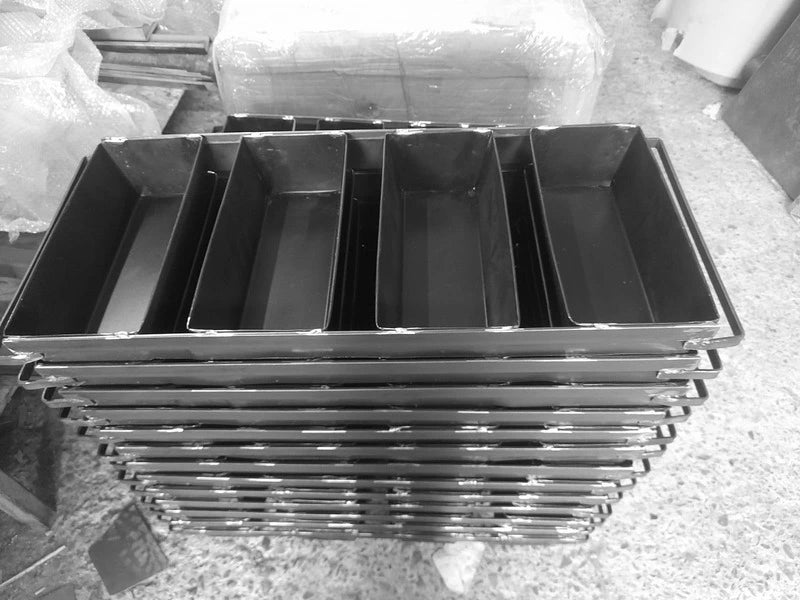 Stivă înaltă de tăvi industriale din tablă neagră pentru coacere la baterie de 4 franzele. Echipamente profesionale robuste destinate brutăriilor de capacitate mare, fotografiate în atelierul de producție înainte de ambalare.
