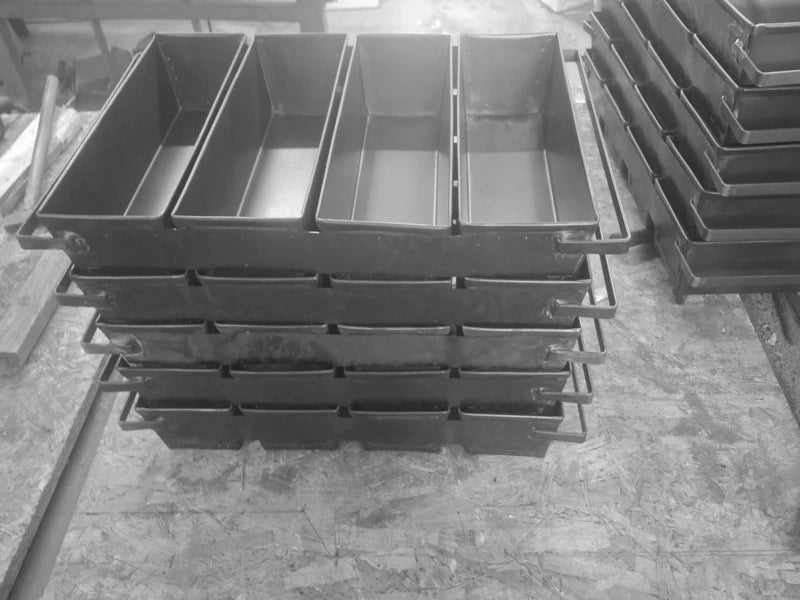Stivă de tăvi profesionale din tablă neagră pentru coacere la baterie de 4. Forme robuste din oțel negru pentru franzele, așezate una peste alta în atelierul de producție, esențiale pentru eficiența din brutării.