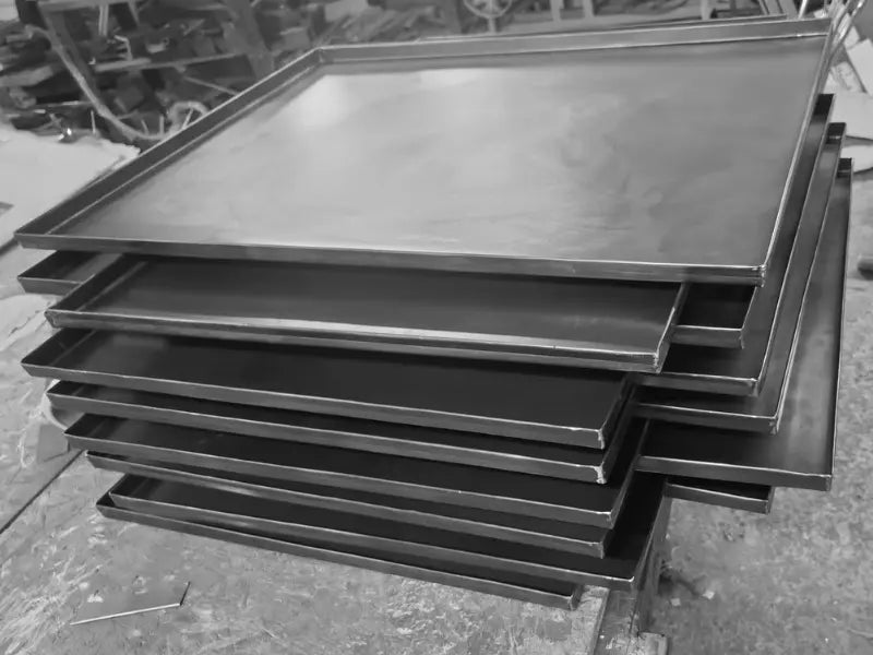 Stivă de tăvi profesionale pentru panificație și patiserie, dimensiune 60x40 cm. Fabricate din tablă neagră (oțel) cu grosimea de 0.8 mm pentru o coacere uniformă în brutării comerciale.