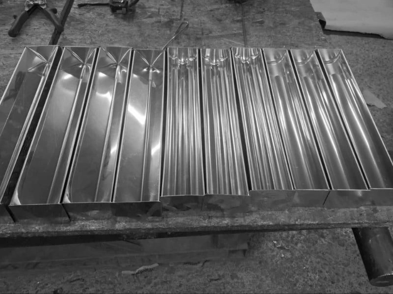 Rânduri de forme și tăvi de terină din inox proaspăt lucrate, aliniate în fabrică înainte de expediere.