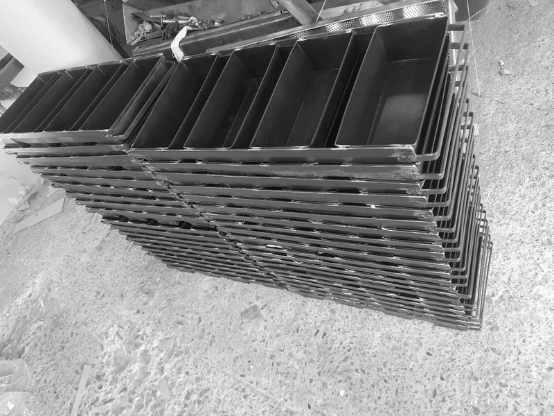 Stoc mare de tăvi profesionale din tablă neagră pentru coacere la baterie de 4. Mai multe stive de forme pentru franzele, pregătite în atelierul de producție pentru echiparea brutăriilor industriale și comerciale.