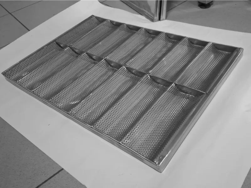 Tavă perforată profesională din inox AISI 304 pentru baghete mici și chifle, prevăzută cu 14 canale. Vedere din unghi a structurii cu orificii de 3 mm, care asigură o coacere uniformă și circulația optimă a aerului în brutării (dimensiune 600x400 mm).