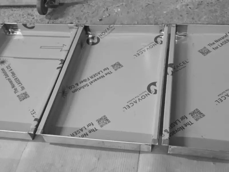 Tăvi profesionale din inox alimentar AISI 304 cu șină, fotografiate în fabrică pe parcursul procesului de producție. Tăvile sunt prevăzute cu folie de protecție pentru a preveni zgârieturile, având dimensiunile 325x530x40mm.