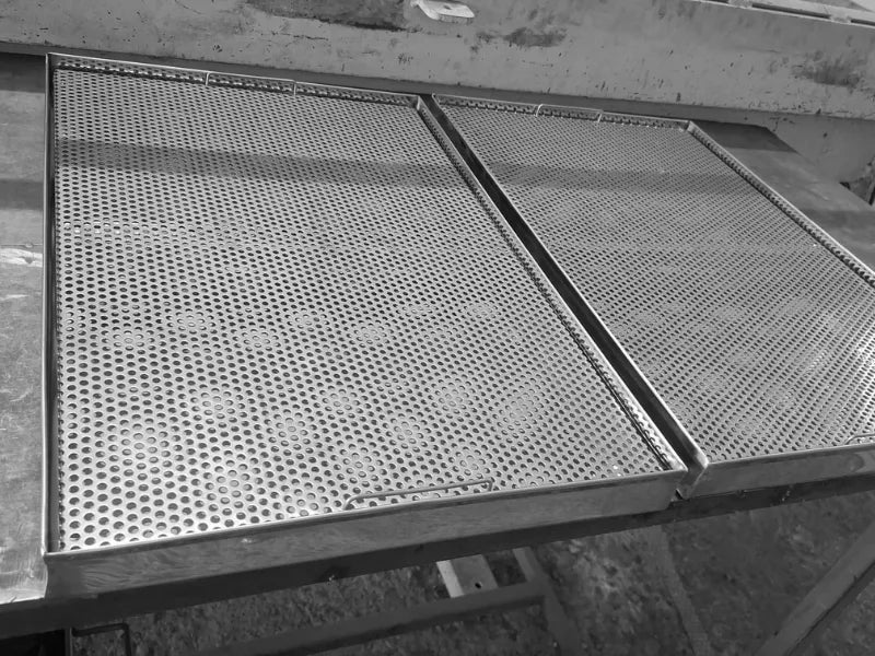 Două tăvi perforate din inox AISI 304 pentru scurgerea paharelor, așezate alăturat pe bancul de lucru din atelier. Imaginea ilustrează perfect designul modular al produsului, permițând extinderea spațiului de uscare în funcție de necesitățile din baruri, restaurante și bucătării HoReCa.