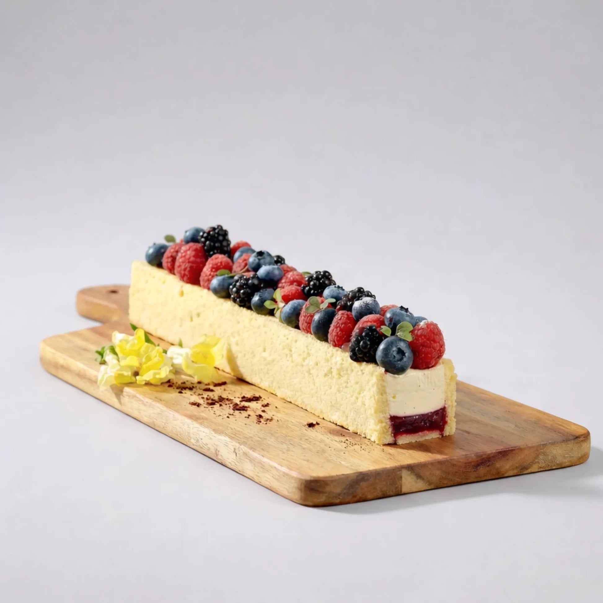 Desert dreptunghiular tip mousse preparat în formă de terină, decorat cu fructe de pădure pe tocător de lemn