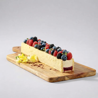 Desert dreptunghiular tip mousse preparat în formă de terină, decorat cu fructe de pădure pe tocător de lemn