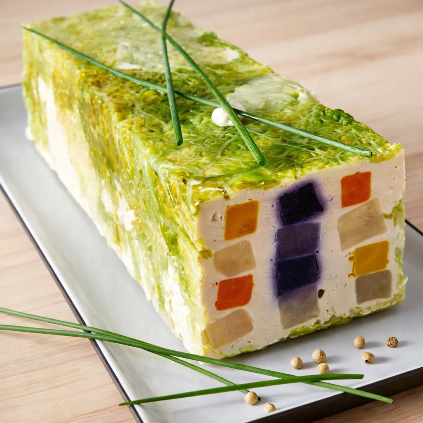 Terină dreptunghiulară tip mozaic cu straturi de legume colorate și ierburi pe platou alb