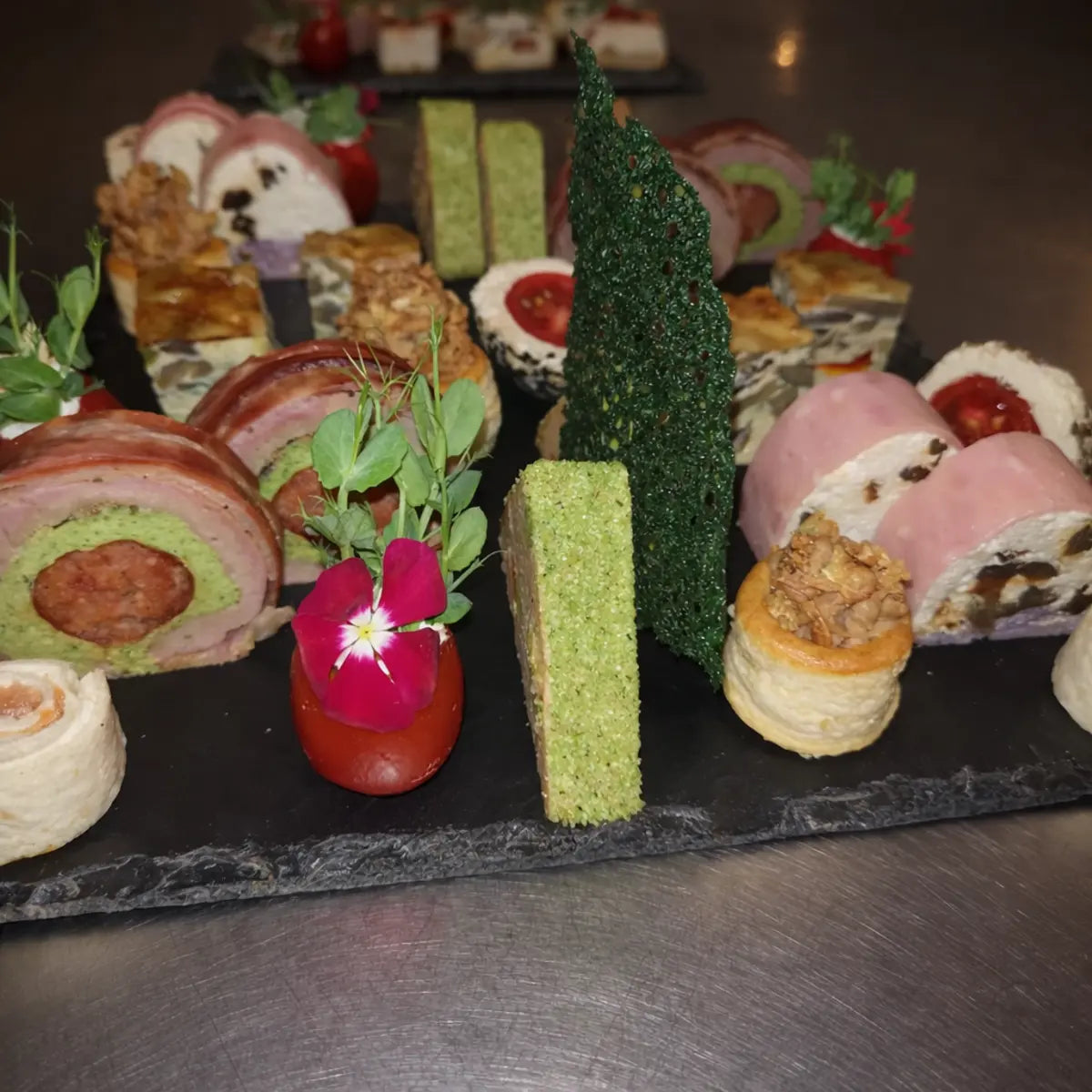 Asortiment de aperitive fine dining și terine cu forme unice, aranjate artistic pe un platou negru din ardezie.